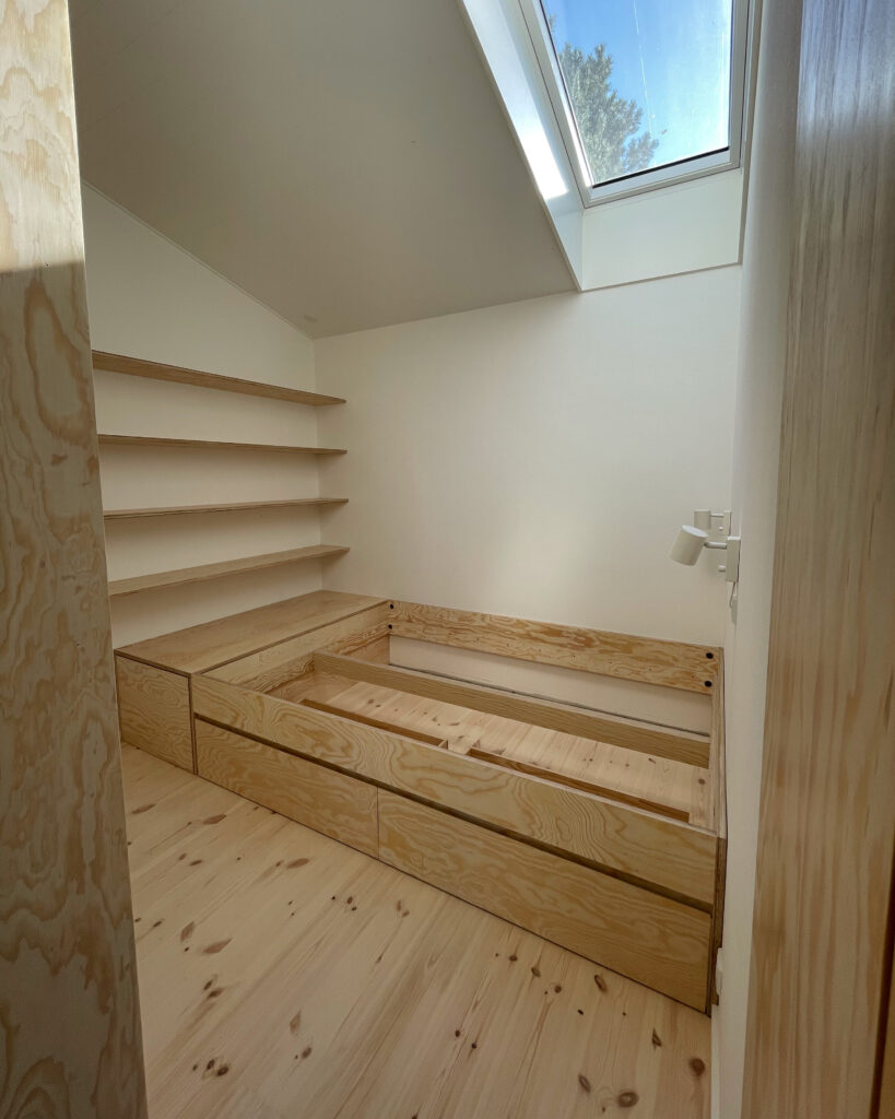 Soveværelse med dobbeltseng, skabe, hylder og gulve i lyst fyrretræ