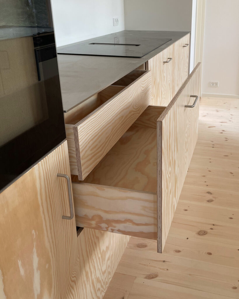 Køkkenalrum i sommerhus med fronter i fyrretræ og bordplade i stål