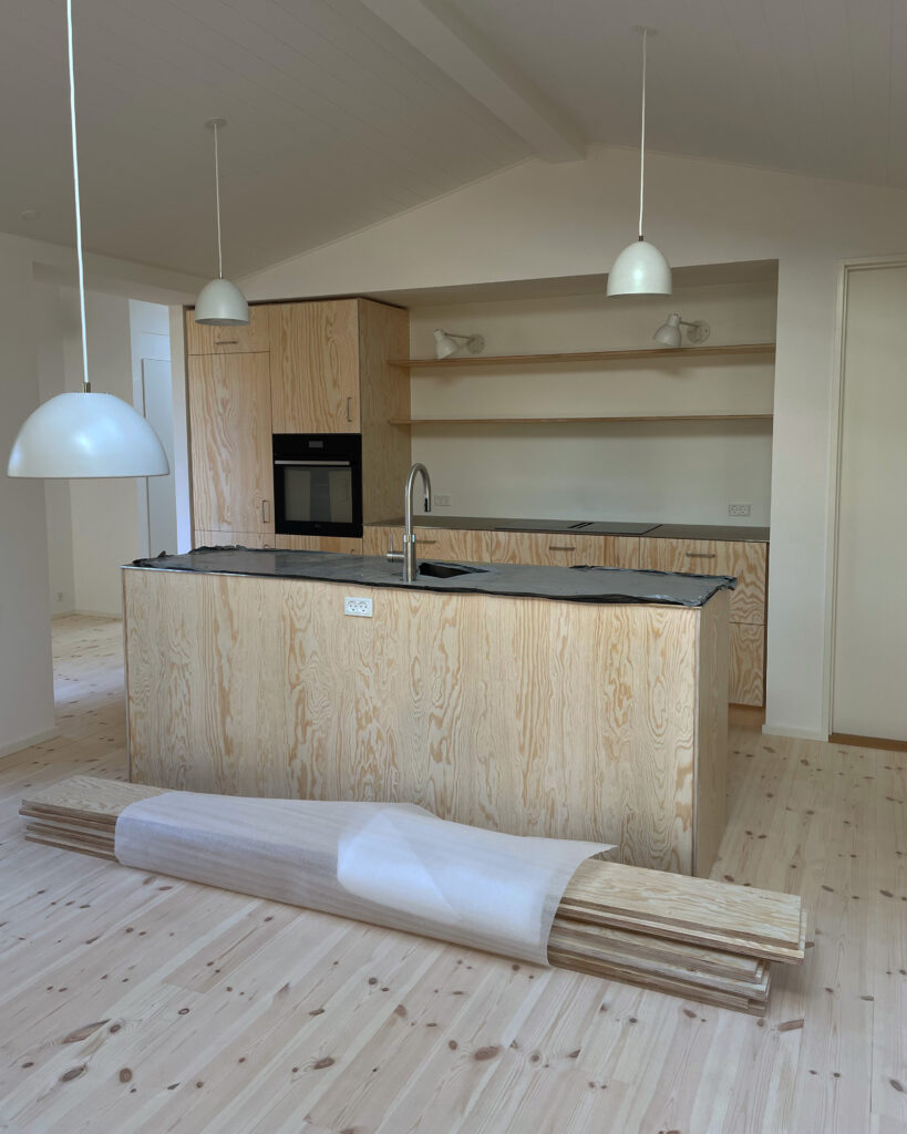 Køkkenalrum i sommerhus med fronter i fyrretræ og bordplade i stål