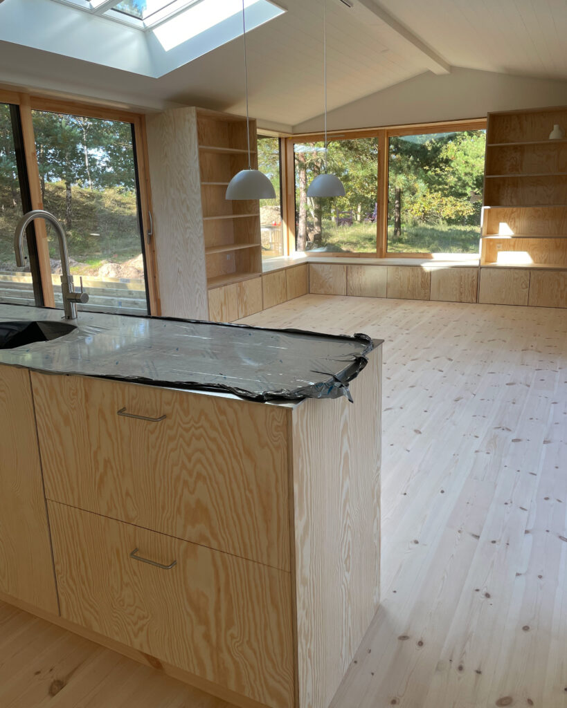 Køkkenalrum i sommerhus med fronter i fyrretræ og bordplade i stål