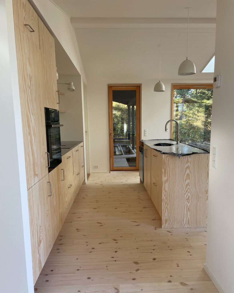 Køkkenalrum i sommerhus med fronter i fyrretræ og bordplade i stål